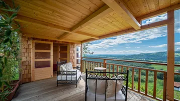 Gemütlicher Holzbalkon mit Sitzgelegenheiten und weitem Blick über die grüne Hügellandschaft.