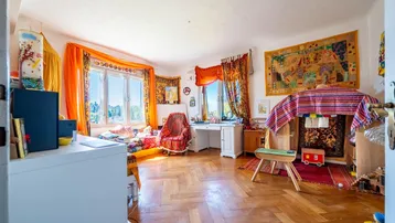 Helles, farbenfrohes Zimmer mit Parkettboden, großen Fenstern und vielfältiger Dekoration.