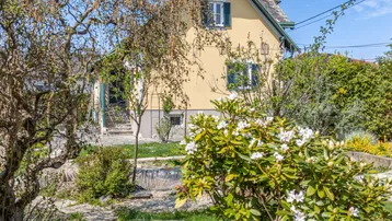 Charmantes Haus mit gelber Fassade, umgeben von einem blühenden Garten mit Bäumen und Sträuchern.