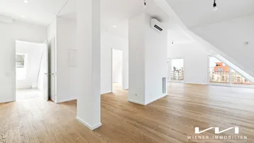 Geräumiger, heller Wohnbereich im Dachgeschoss mit Holzboden, hohen Decken und Zugang zu einem Balkon.