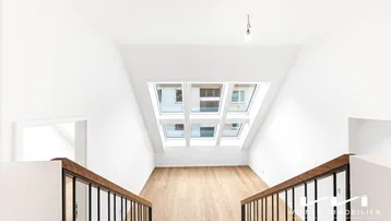 Heller Dachbodenbereich mit großen Dachfenstern, Holzfußboden und moderner Treppe.