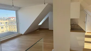 Heller offener Wohnbereich mit Holzboden, Dachschrägen und Zugang zum Balkon.
