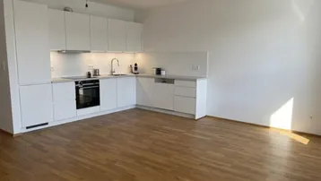Moderne weiße Einbauküche mit Holzboden in einem hellen, leeren Raum.