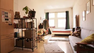 Helles und funktionales Studio-Apartment mit Schlaf-, Wohn- und Arbeitsbereich sowie integriertem Kühlschrank.