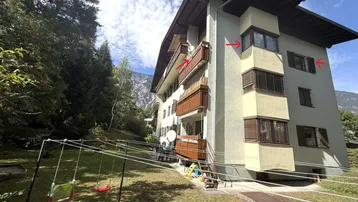 Mehrfamilienhaus mit Balkonen, umgeben von Bäumen und einem kleinen Spielbereich im Garten.