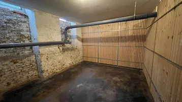 Geräumiger Kellerraum mit unverputzten Ziegelwänden, Holzverkleidung und sichtbaren Rohren an der Decke.