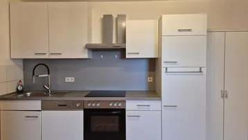 Moderne Einbauküche mit weißen Schränken, integrierten Geräten und grauer Rückwand.