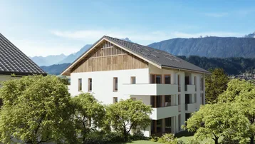 Modernes Mehrfamilienhaus mit Balkonen und Holzfassadenelementen vor einer beeindruckenden Bergkulisse.