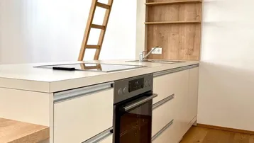 Moderne Küchenzeile mit integriertem Backofen, Induktionskochfeld und Holzregalen, ergänzt durch eine Leiter zu einer oberen Ebene.