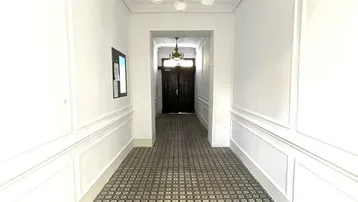 Langer Flur mit gemustertem Fliesenboden, Stuckdecke und klassischer Deckenleuchte in einem Altbau.