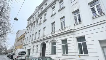 Klassisches Mehrfamilienhaus mit weißer Fassade und vielen Fenstern an einer Kopfsteinpflasterstraße.