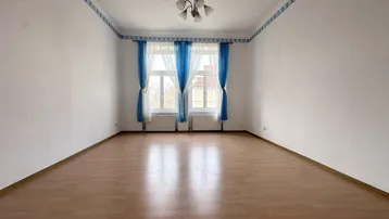 Helles, leeres Zimmer mit Parkettboden, weißen Wänden und blauen Vorhängen an den Fenstern.