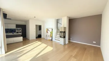 Heller offener Wohnbereich mit Holzboden, Kamin und integrierter Küche, ideal für modernes Wohnen.