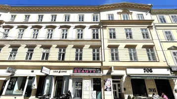Historisches Gebäude mit mehreren Geschäften im Erdgeschoss und Wohnungen darüber, unter blauem Himmel.