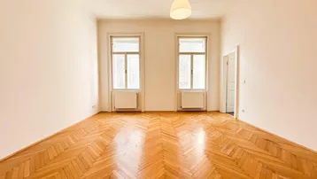Helles Zimmer mit Fischgrätparkettboden und zwei großen Fenstern, bereit zur individuellen Gestaltung.