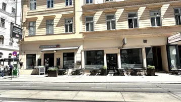 Fassade eines historischen Gebäudes mit Geschäften und Restaurants im Erdgeschoss an einer belebten Straße.