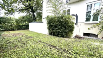 Gartenbereich neben dem Gebäude mit Rasenfläche und üppiger Bepflanzung, ideal für Entspannung im Freien.