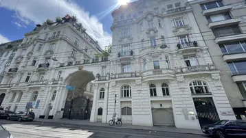 Prächtiges historisches Gebäude mit aufwendiger Fassade und großem Torbogen an einer sonnigen Straße.