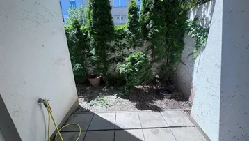 Kleiner, gepflasterter Gartenbereich mit hohen Hecken und einem Wasseranschluss.