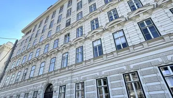 Klassisches Wiener Altbaugebäude mit eleganter Fassade und vielen Fenstern unter blauem Himmel.