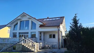 Modernes Einfamilienhaus mit großen Fenstern, Satteldach und einer Außentreppe zum Garten.