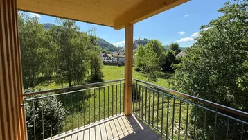 Heller Balkon mit Holzboden und Geländer, bietet einen weiten Blick auf die grüne Landschaft und Berge.