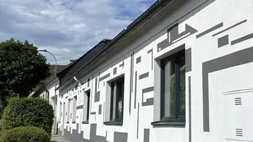 Moderne Fassade eines Gebäudes mit auffälligen geometrischen Mustern und dunklen Fenstern unter blauem Himmel.