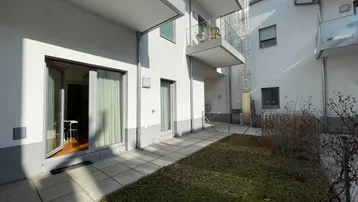 Helle Erdgeschoss-Terrasse mit direktem Zugang zur Wohnung, umgeben von moderner Architektur und Grünfläche.