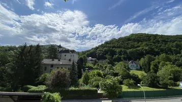 Weitläufiger Blick über eine grüne Hügellandschaft mit vereinzelten Häusern und einem historischen Gebäude.
