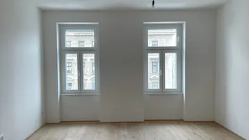 Helles, leeres Zimmer mit zwei Fenstern und neuem Parkettboden, bereit zur individuellen Einrichtung.