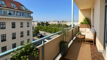 Möblierter Balkon mit Pflanzen und weitem Blick über die Stadt und grüne Alleen.