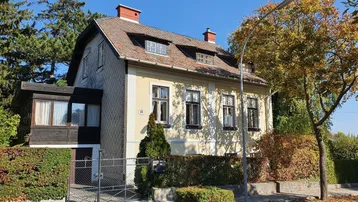 Charmantes Einfamilienhaus mit traditioneller Architektur, umgeben von einem gepflegten Vorgarten und Bäumen.