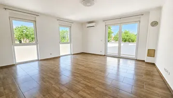 Helles Wohnzimmer mit Fliesenboden, großen Fenstern und Zugang zu einem Balkon.