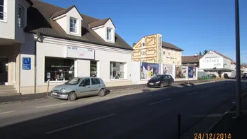 Straßenansicht mit Gebäuden, geparkten Autos und Geschäften unter blauem Himmel.