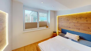 Gemütliches Schlafzimmer mit Holzakzentwand, indirekter Beleuchtung und Fenster mit Plissees.