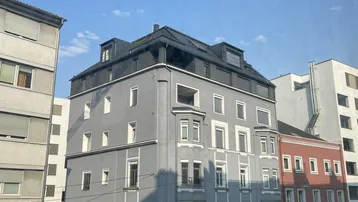 Ansicht eines Eckgebäudes in der Stadt mit mehreren Stockwerken und Fenstern unter blauem Himmel.