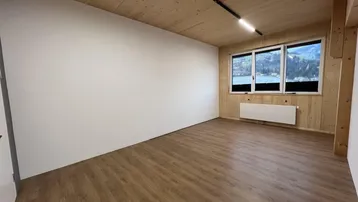 Heller Raum mit Holzwänden und -decke, Laminatboden und Fenstern mit Blick auf einen See oder Fluss.