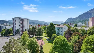 Panoramablick auf die Stadt, umliegende Berge und einen Spielplatz mit viel Grün.