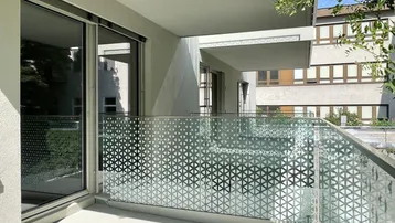 Moderner Balkon mit Glasgeländer und geometrischem Muster, bietet einen Blick auf die Umgebung.