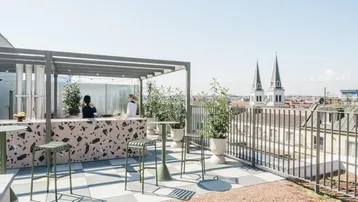 Moderne Dachterrasse mit Bar, Sitzgelegenheiten und weitem Blick über die Stadt mit Kirchtürmen.