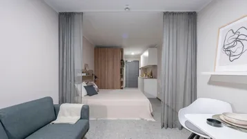 Helles Studio-Apartment mit modernem Sofa, Essbereich und abgetrenntem Schlafbereich durch Vorhänge.