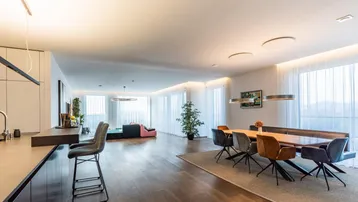 Geräumiger, offener Wohn- und Essbereich mit Holzboden, großen Fenstern und moderner Einrichtung.