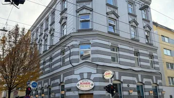 Historisches Eckgebäude mit markanter Fassade und Geschäften im Erdgeschoss an einer belebten Kreuzung.