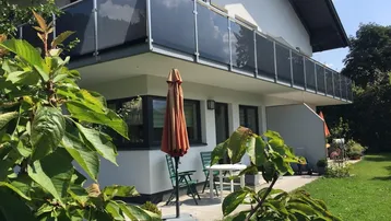 Außenansicht des Hauses mit modernem Balkon und einer möblierten Terrasse im Grünen.