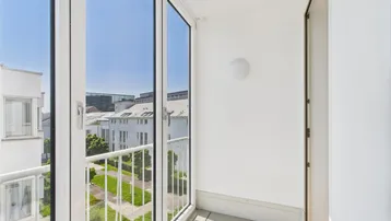 Heller Balkon mit Blick auf den begrünten Innenhof und die umliegenden Gebäude.