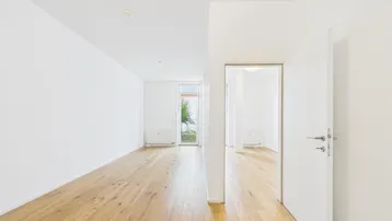 Helles, leeres Zimmer mit Holzboden und Zugang zu einem kleinen Außenbereich.
