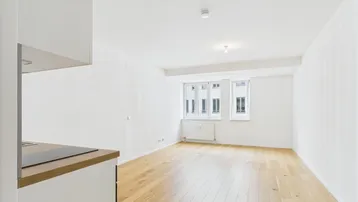 Helles Wohnzimmer mit Holzboden und integrierter Küchenzeile, bietet vielseitige Nutzungsmöglichkeiten.