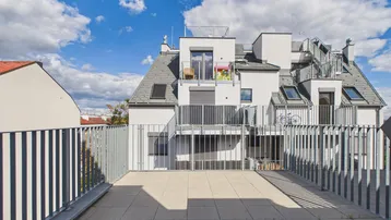 Große geflieste Terrasse mit Blick auf ein modernes Wohngebäude und den Himmel.