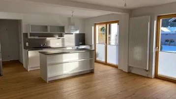 Helle, offene Wohnküche mit Kücheninsel, Holzboden und Zugang zum Außenbereich durch große Terrassentüren.