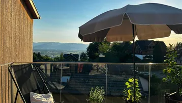 Gemütlicher Balkon mit Sitzgelegenheiten, Pflanzen und weitem Blick über die Landschaft bei Sonnenuntergang.